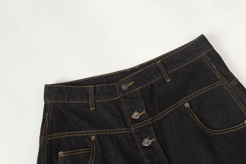 Close-up of black denim waistband and asymmetric button front with orange stitching