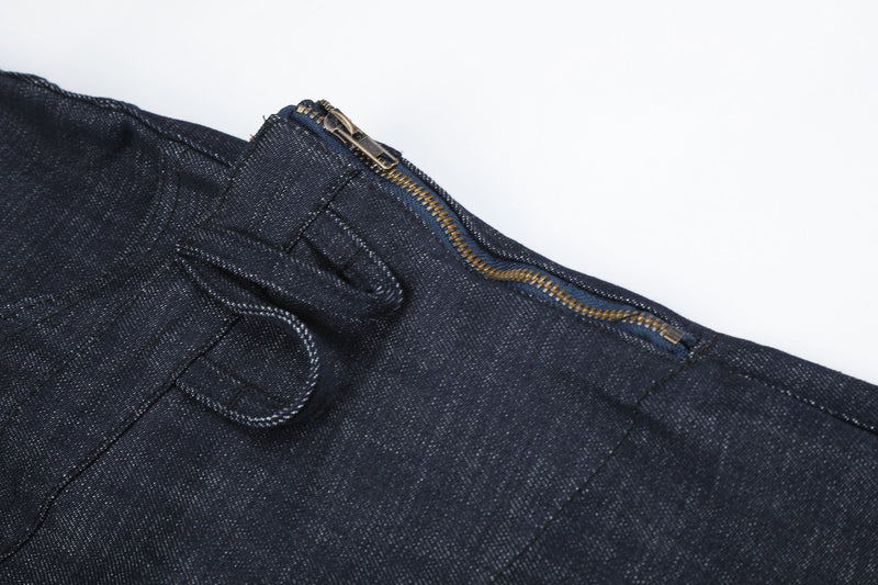 Close-up of dark denim side waistband with exposed brass zipper and pull tab