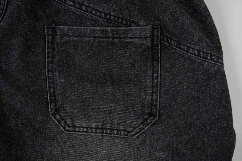 Close-up of black denim back pocket with stitched edges on layered plaid jeans