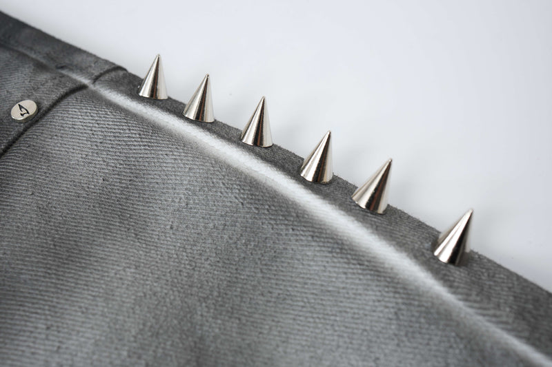 Close-up of silver cone spikes mounted along a gray denim side seam