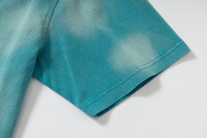 Close-up of a teal washed vintage tee sleeve with abstract faded dye and visible hem stitching