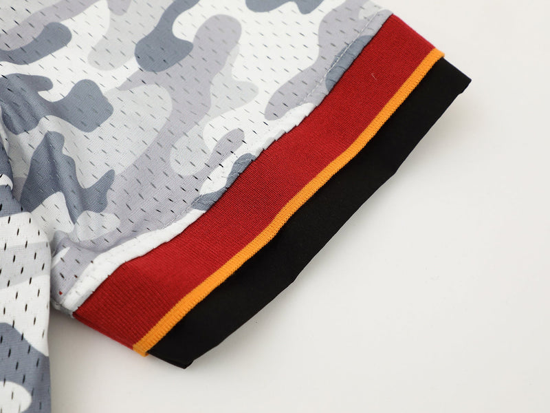 Close-up of a gray camo mesh shirt sleeve with red, orange, and black ribbed cuff details on a white background