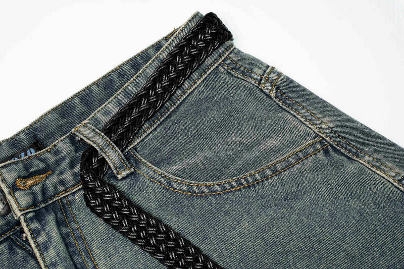 Close-up of blue jeans waistband with black braided belt detail and belt loop