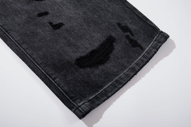 Close-up of hem on deep charcoal jeans with distressed rip and frayed detail