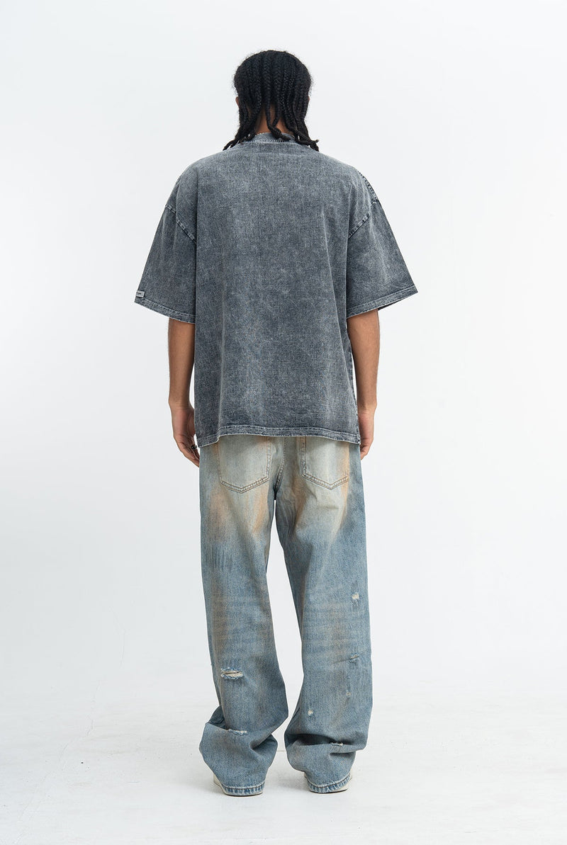Back view of a faded gray vintage washed graphic tee styled with loose distressed jeans on a model against a white background