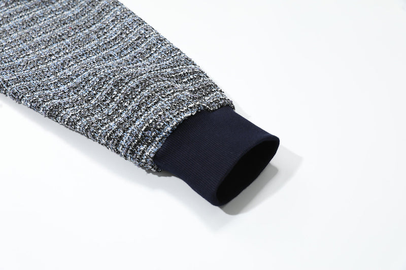 Close-up of a sleeve cuff with dark ribbed trim and speckled boucle knit fabric