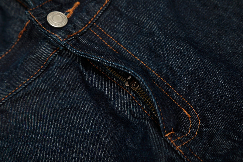 Close-up of the front zipper and layered waist seam on deep indigo jeans