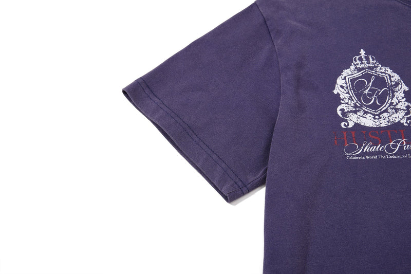 Purple washed crewneck tee with vintage crest graphic and text print on the chest, shown on a white background