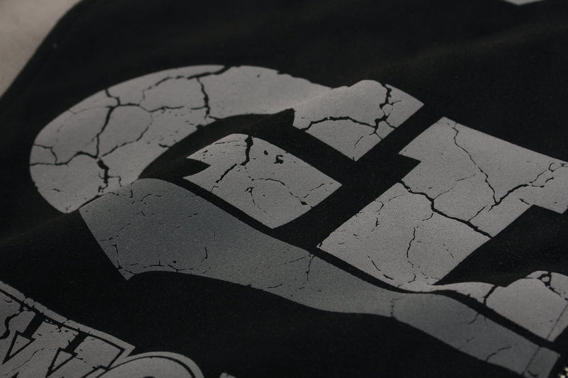 Close-up of cracked gray front lettering on black hoodie, showing part of the GLFS print