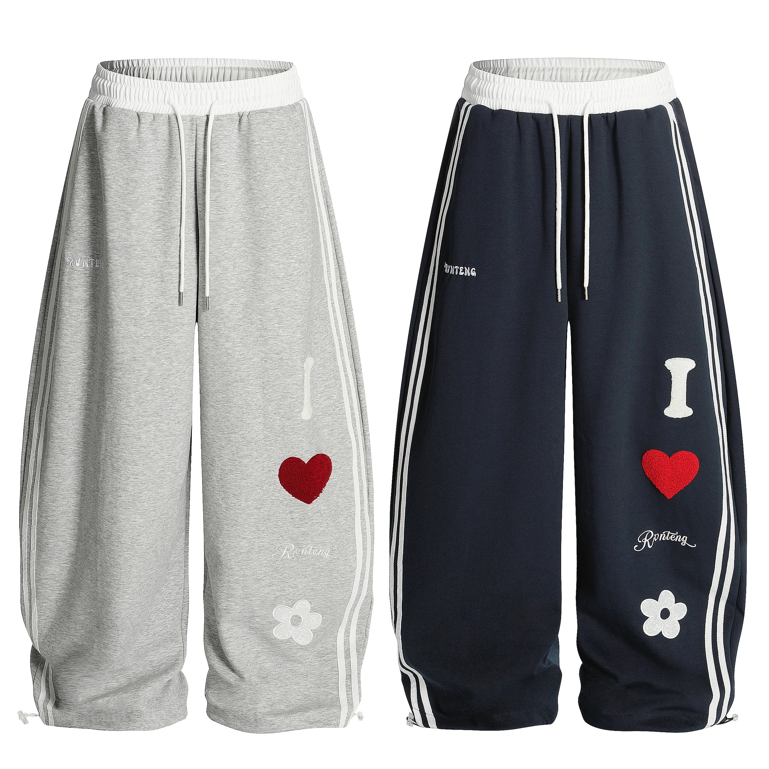 Grey and navy wide-leg track pants with chenille heart patch, daisy embroidery, and dual white side stripes