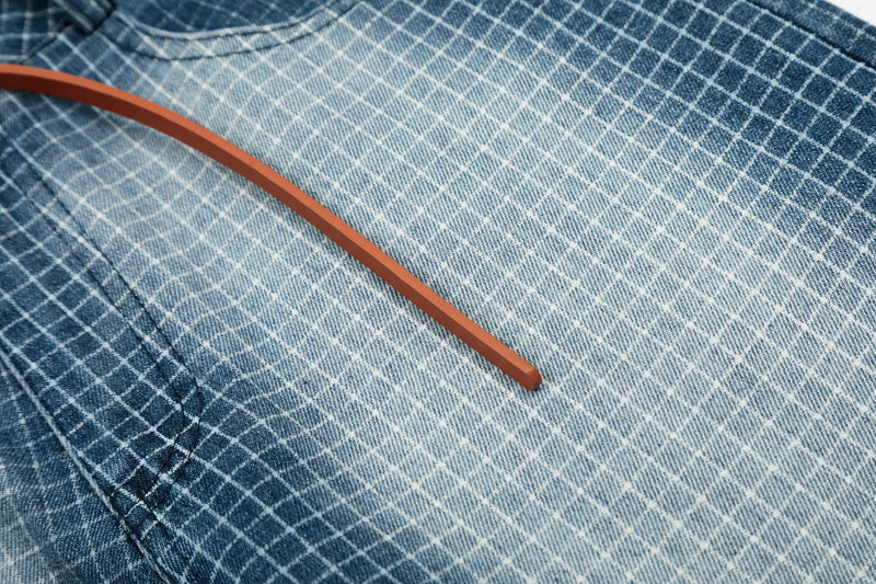 Close-up of side belt strap across faded blue grid denim shorts