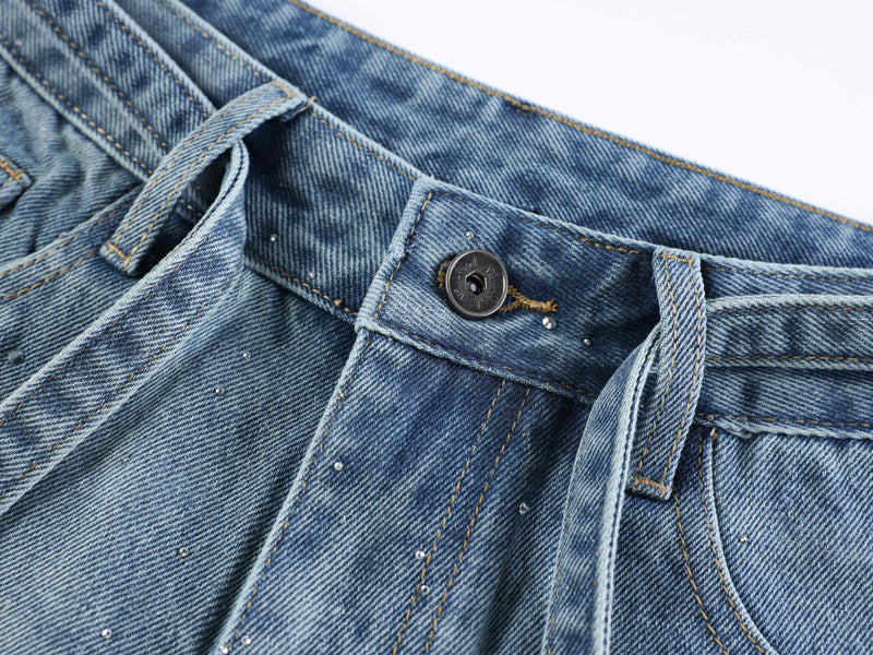 Light blue denim waistband close-up with button, belt loop, and rhinestone details