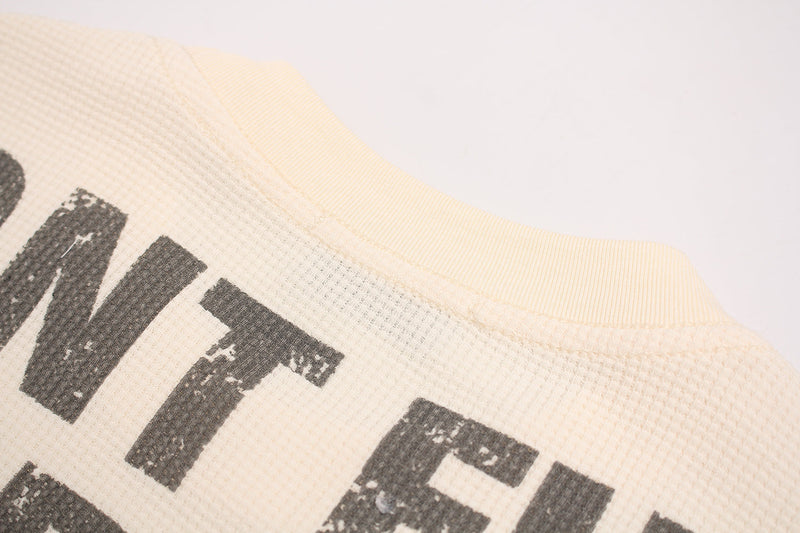 Close-up of cream waffle knit tee with distressed black streetwear graphic and ribbed collar seam