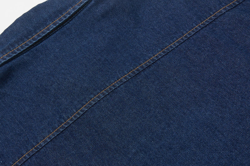 Close-up of dark blue denim shirt fabric with diagonal tan stitching and clean seam details