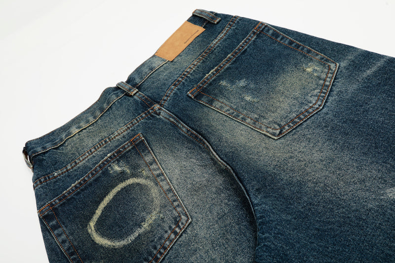 Back pocket close-up on dark blue wide-leg jeans with paint-splatter fading