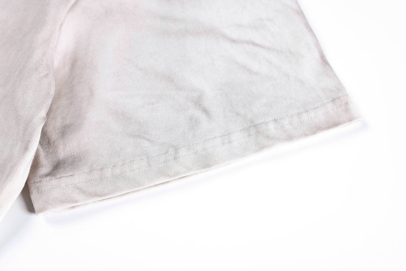 Close-up of a washed vintage tee sleeve hem in light beige with subtle faded texture and stitched detail