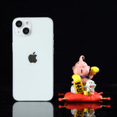 A white smartphone with an Apple logo stands upright on the left, while to the right, a Seakoff Majin Buu Collectible Figure from Dragon Ball Z&