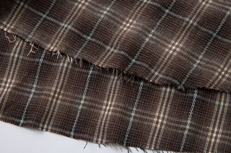 Frayed hem detail on brown plaid shirt with worn edges