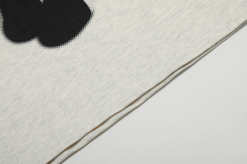 Close-up of an oversized cream graphic tee with black print and visible hem detail on the fabric edge