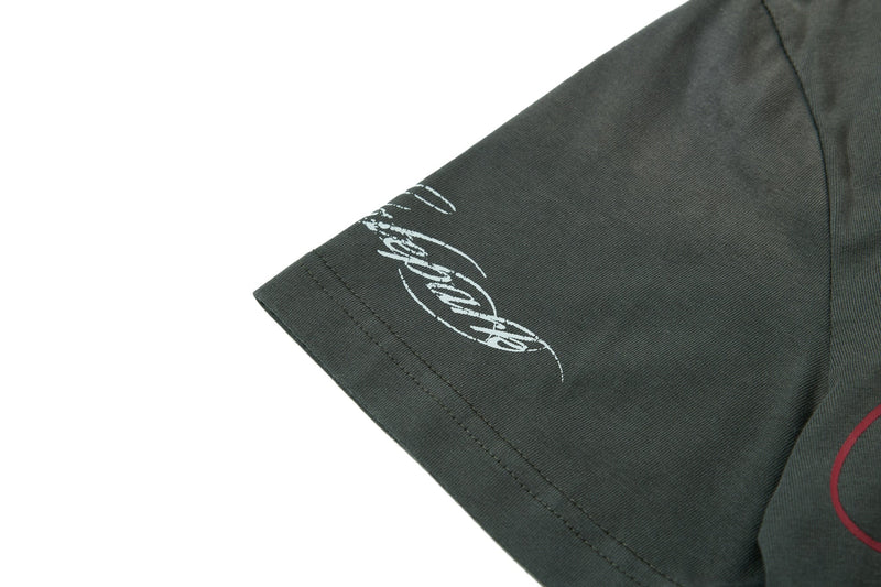 Close-up of dark green vintage graphic polo tee sleeve with white printed lettering and red accent detail