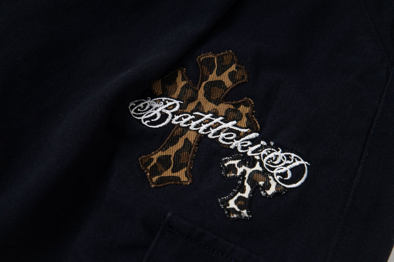 Leopard cross patch with embroidered script on black cargo pants, close-up