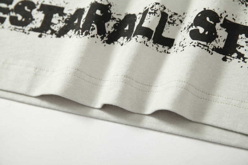 Close-up of a distressed off-white raglan graphic tee with bold black underground streetwear print and raw hem detail
