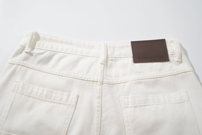 Close-up of the waistband on white jeans with belt loops, button, and brown label