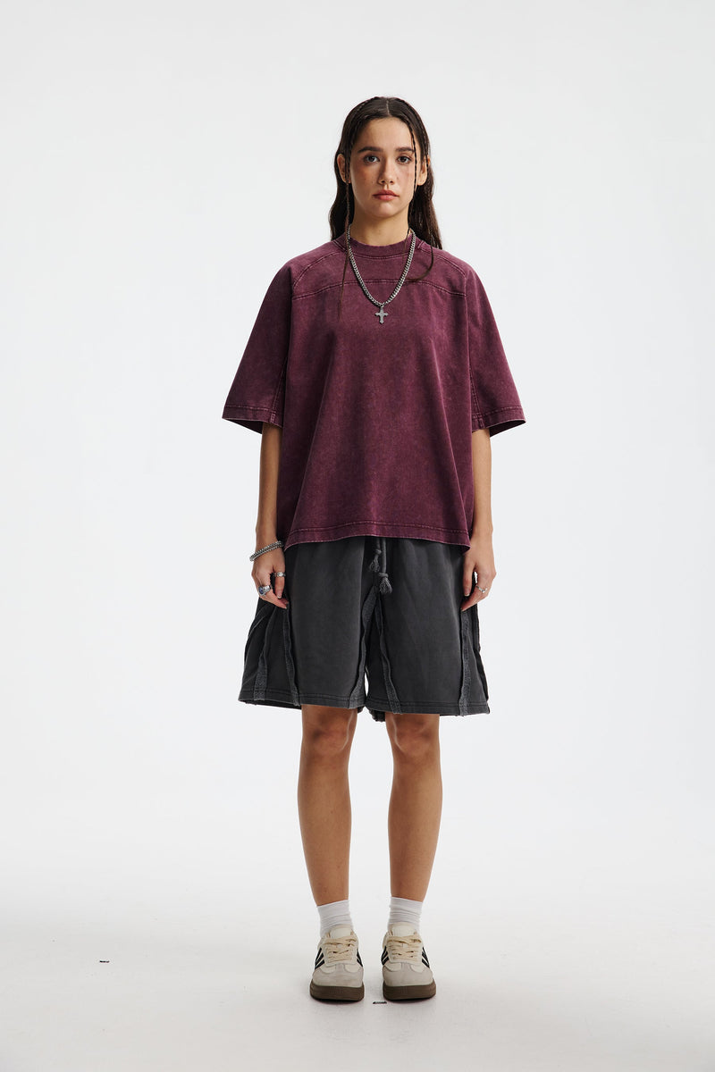 Model wearing a washed burgundy oversized cotton T-shirt with relaxed streetwear fit, styled with black shorts and sneakers