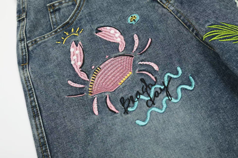 Close-up of crab embroidery and beach graphic text on blue denim jeans