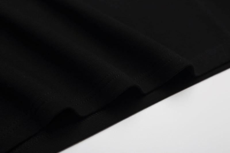 Close-up of black polo shirt fabric with subtle stitched detailing and a clean diagonal fold on white background