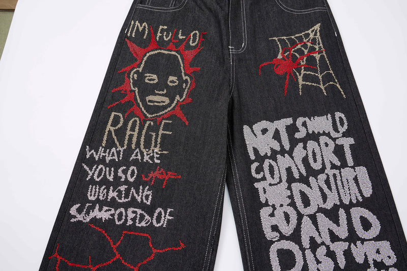 Front view of black denim pants with bold rhinestone graffiti text and face graphics