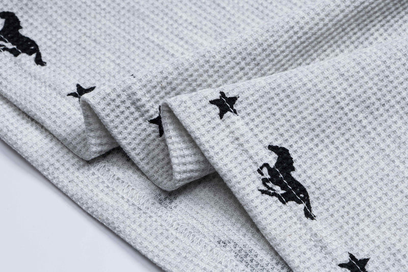 Close-up of light gray waffle-knit polo fabric with black embroidered horse graphics and folded cuff detail