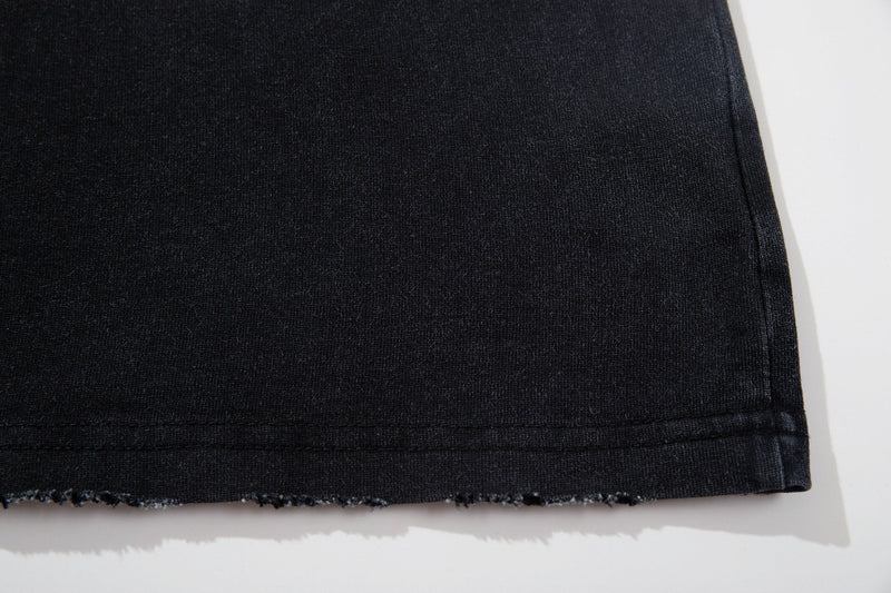 Close-up of a vintage dark washed graphic tee hem with distressed raw edge and subtle black fade