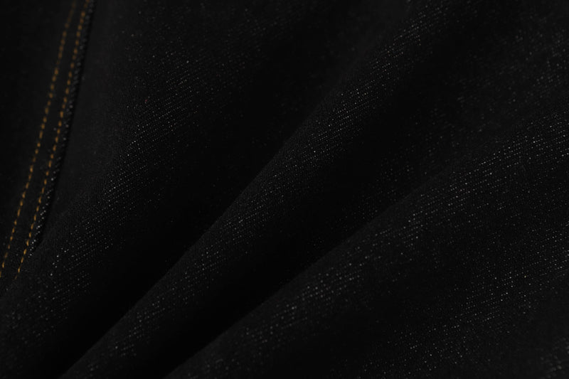 Extreme close-up of black denim fabric with visible weave and orange seam stitching