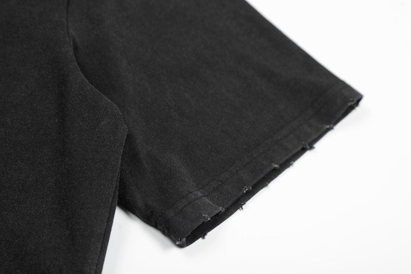 Black distressed graphic tee sleeve detail with raw-cut hem, showcasing punk streetwear style and textured cotton fabric