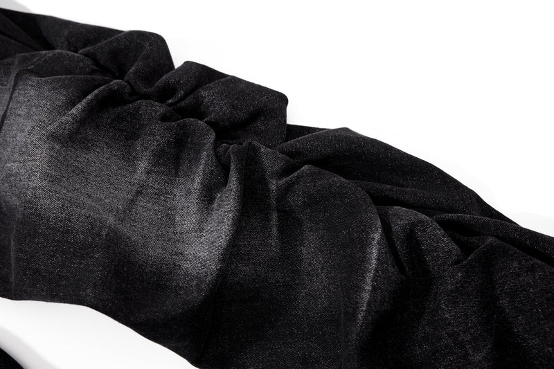Stacked black denim leg close-up with heavy ruched folds