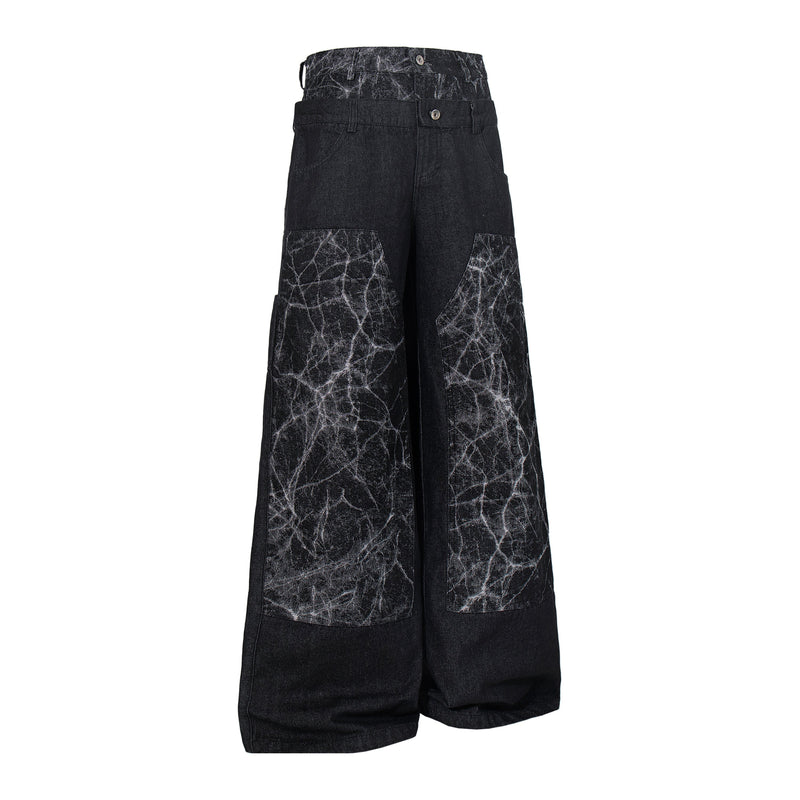 Angled front view of black wide-leg denim pants with cracked panel accents and button fly