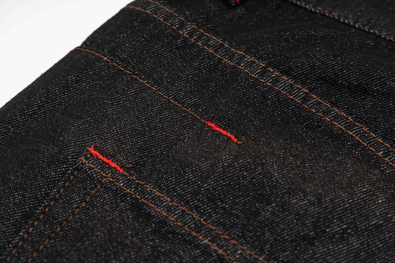 Close-up of dark wash denim with red contrast bar tacks and stitching