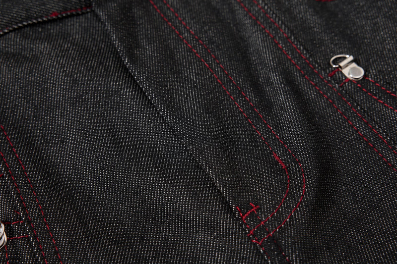 Close-up of black denim side pocket seam with red contrast stitching and silver rivet