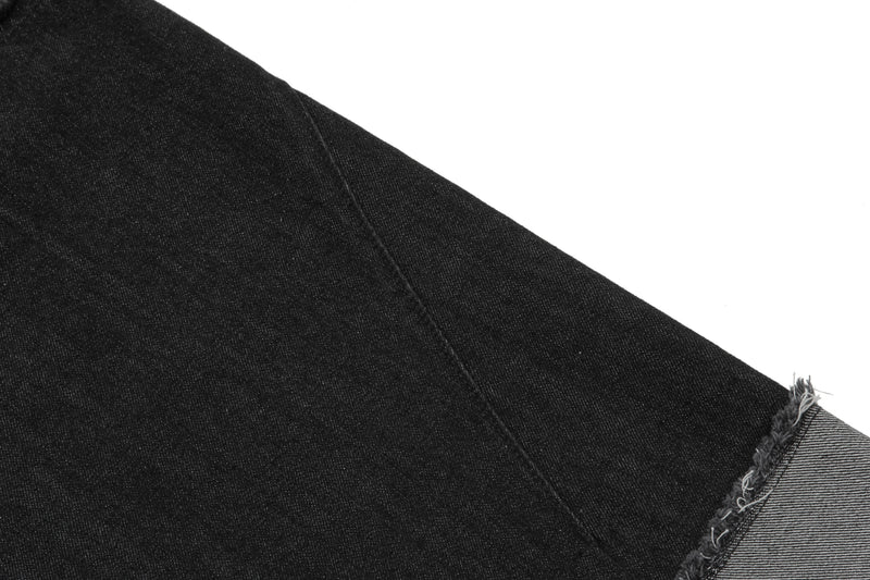 Close-up of black denim shorts leg panel with visible seam and raw hem edge