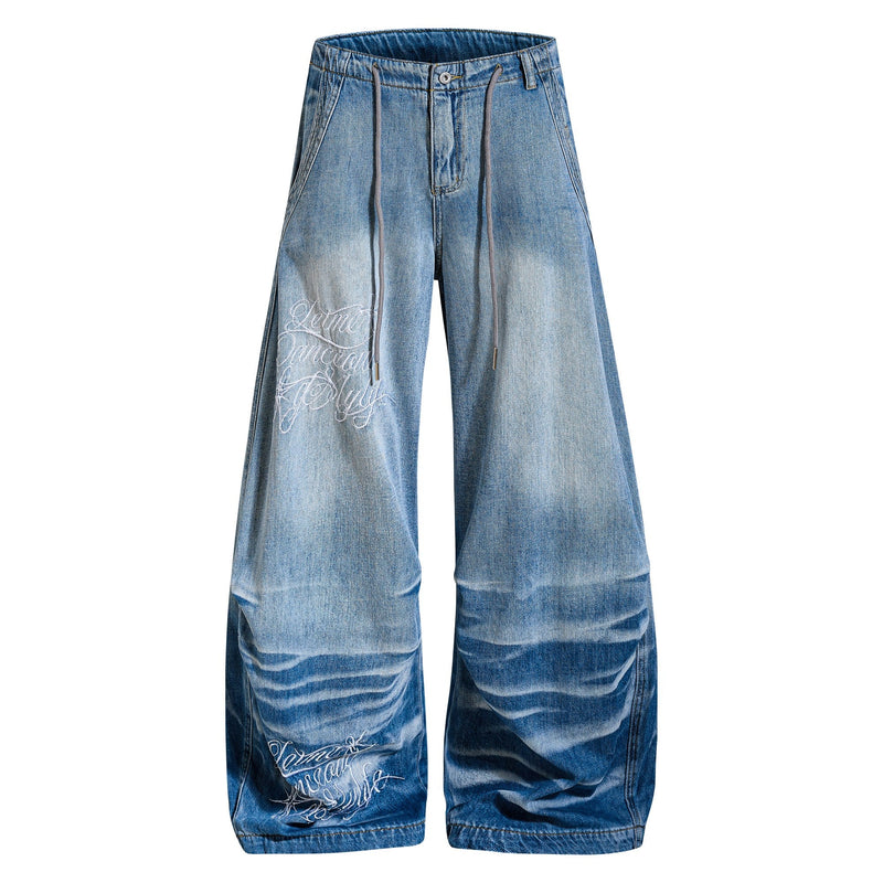 Front view of light wash baggy jeans with drawstring waist and white script graphic on the leg