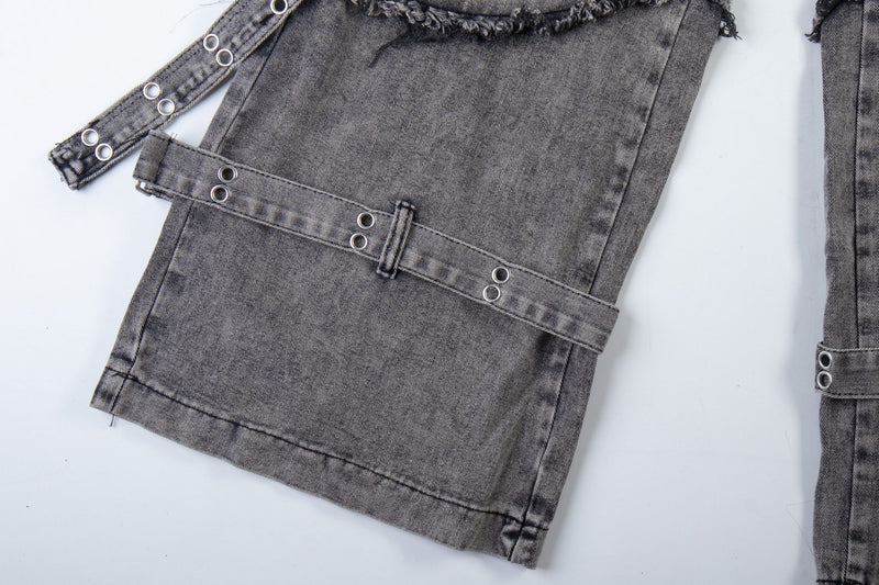 Lower leg close-up of washed black jeans with wraparound strap and metal eyelets