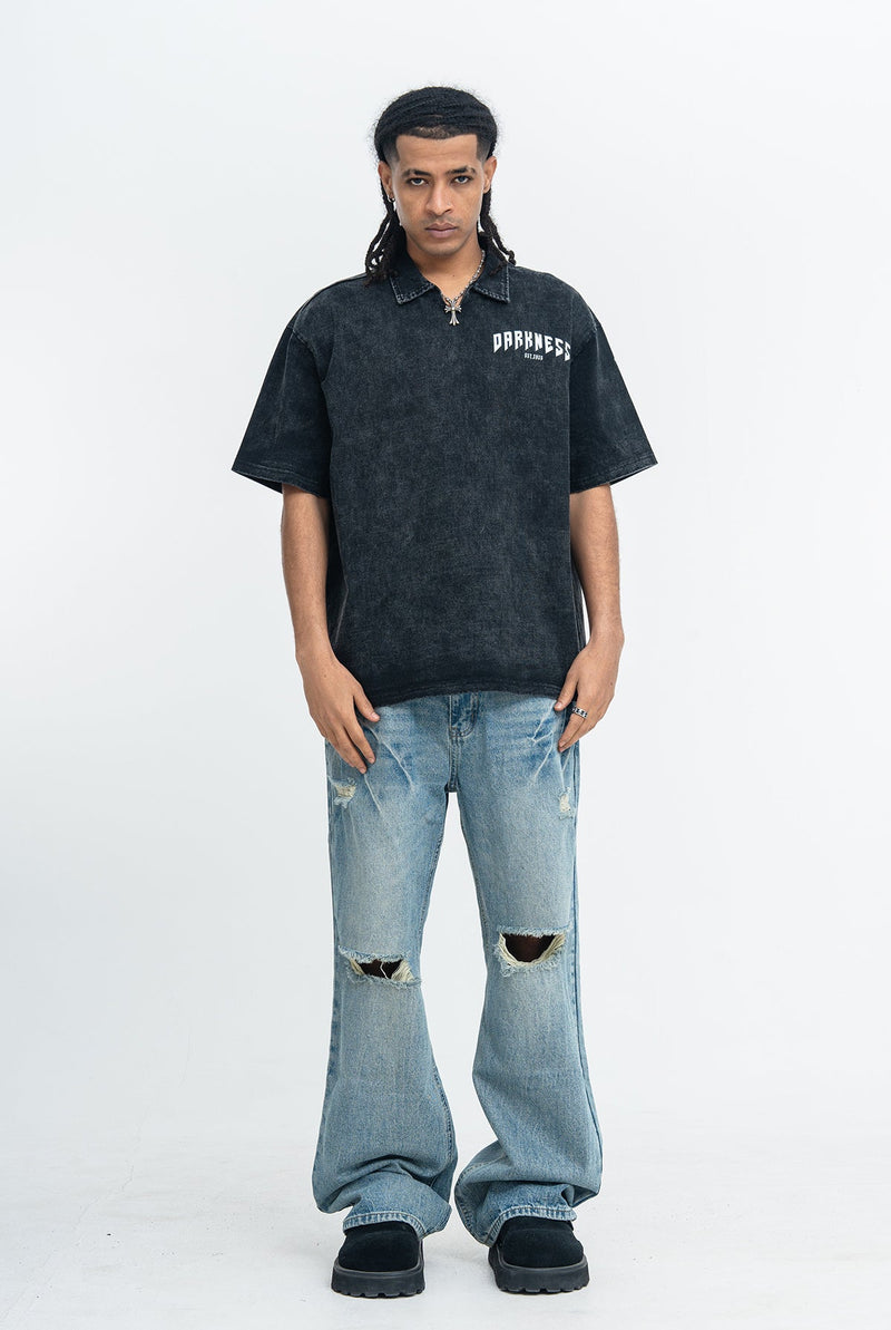 Model wearing a washed black polo shirt with Darkness logo, paired with light distressed wide-leg jeans and black shoes