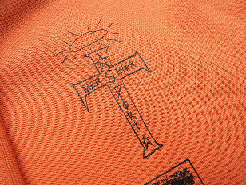 Close-up of cross graphic print with See The Whole World text on orange hoodie