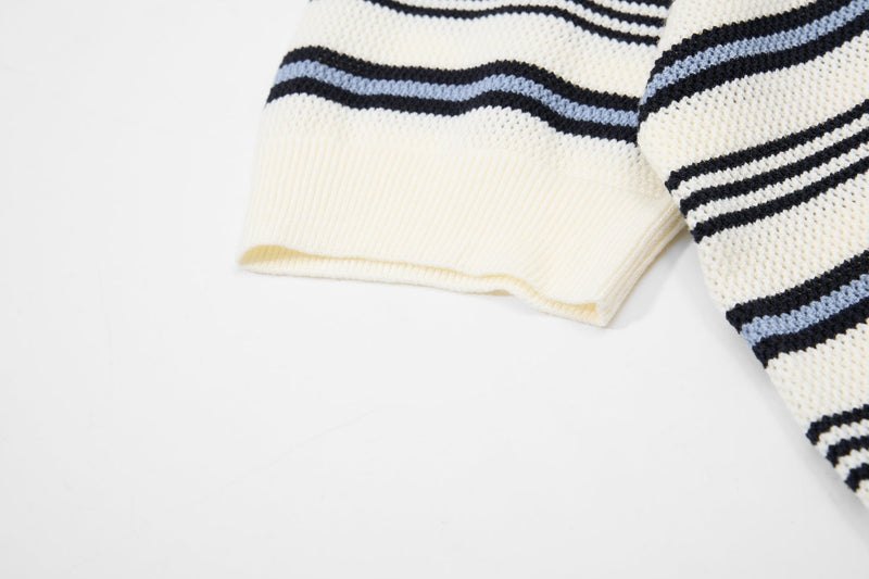 Close-up of a cream knit polo sleeve with navy and light blue retro stripes on soft cotton texture