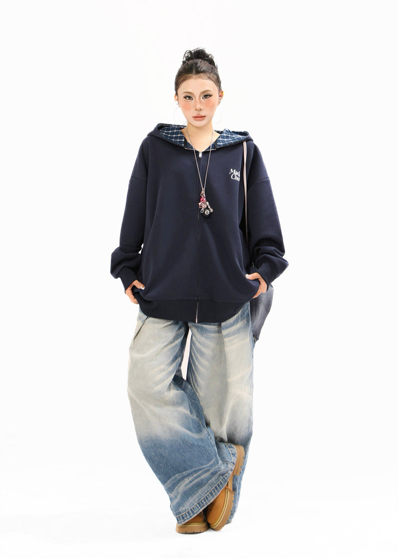 Full-length view of a model wearing a navy zip-up hoodie with plaid hood lining and loose jeans