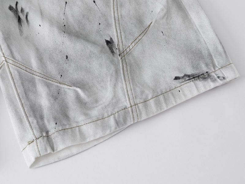 Close-up of the hem on white denim shorts with distressed black splatter detail