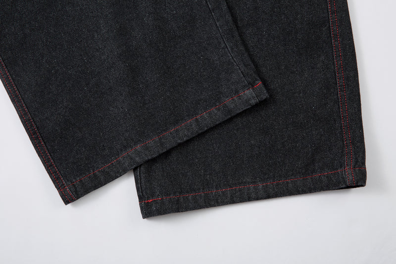 Close-up of the wide leg hems with red stitching on black jeans