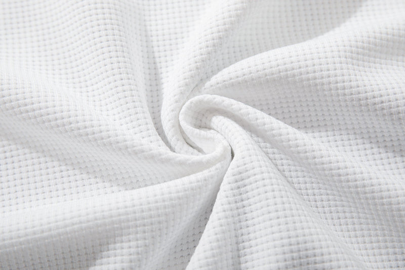 Close-up of white waffle-knit fabric with a soft textured weave and folded drape, likely a graphic tee material