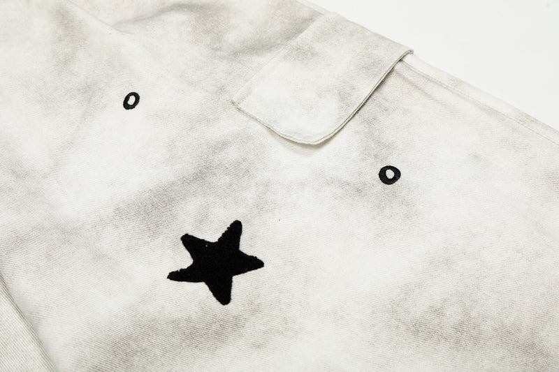 Close-up of black star patch and embroidered dot details on white washed pants